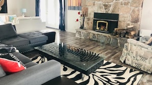 A living room with a stone fireplace, a sofa, a patterned coffee table, and a zebra print rug. - Lake Sparrow Guest House Inc (Severn Bridge)