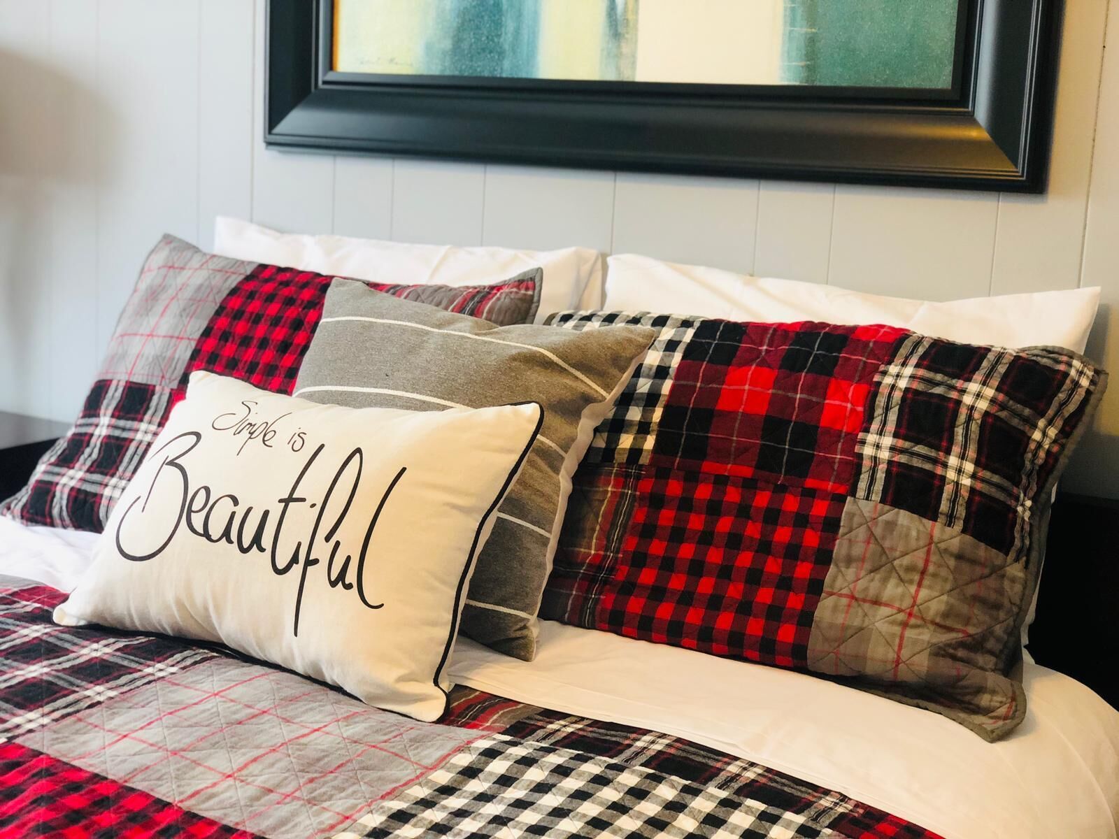 A bed with a plaid-patterned bedspread and multiple pillows, one with the text "Triple is Beautiful."