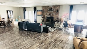 A spacious living room with a stone fireplace, dark wooden flooring, and a large sofa. - Lake Sparrow Guest House Inc (Severn Bridge)