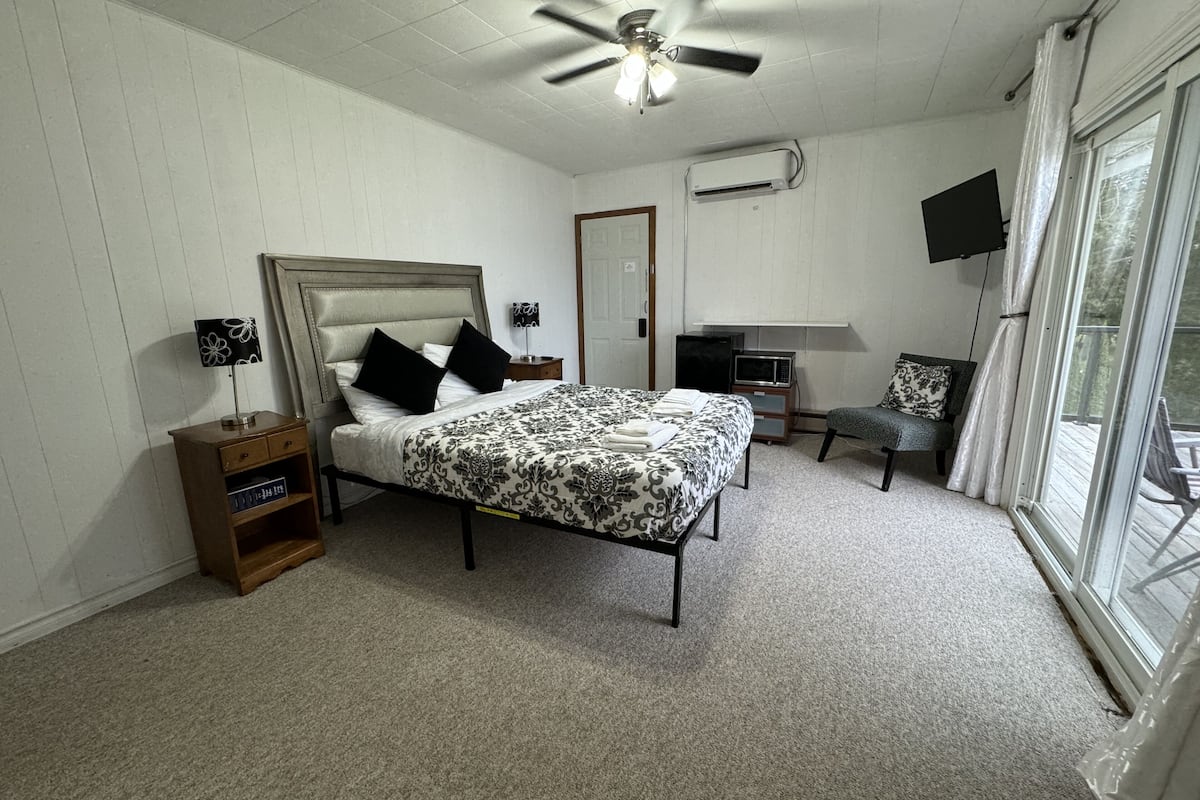 A bedroom with a bed, a desk, a chair, a ceiling fan, and a TV.