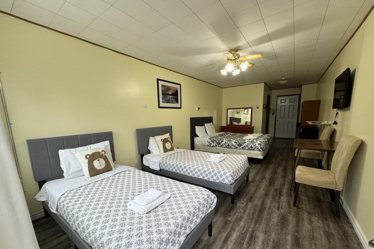 A hotel room with three beds, a ceiling fan, a mirror, and a desk with a chair.