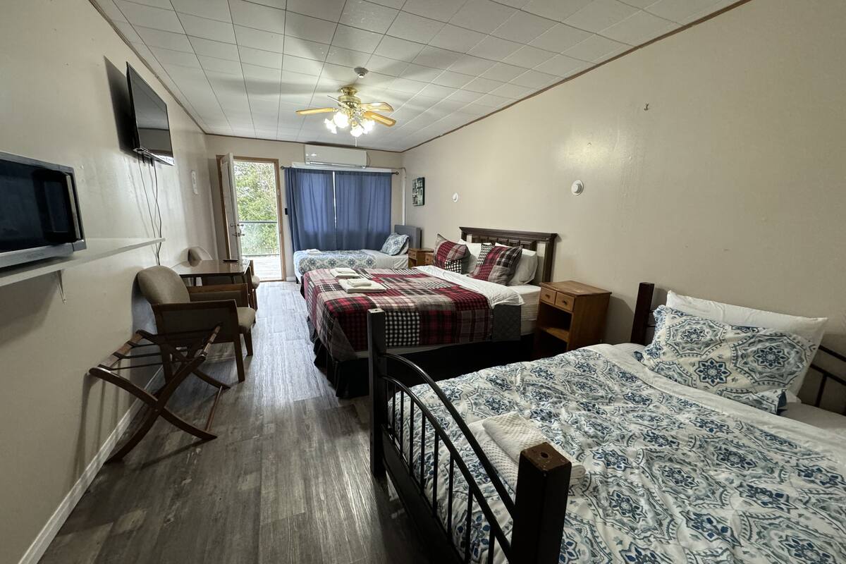 A room with two beds, a desk, a chair, a television, and a ceiling fan.