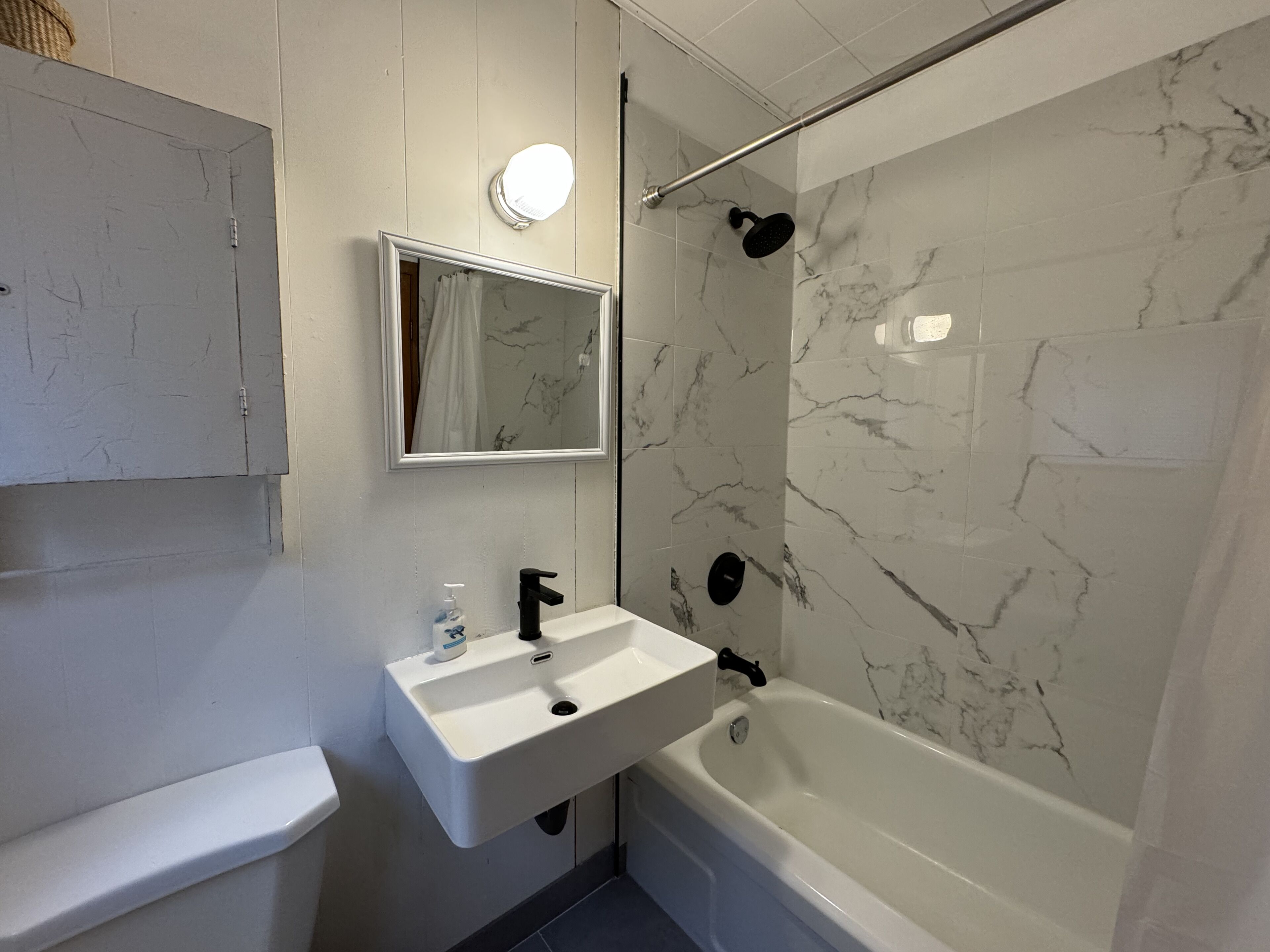 Un baño con lavamanos blanco, espejo, ducha con puerta de cristal y paredes con diseño de mármol.