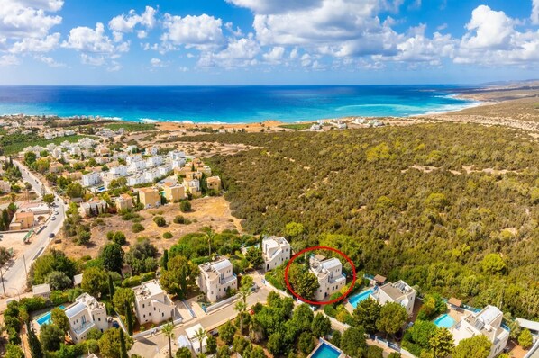 An aerial view of a coastal residential area with houses, a swimming pool, and a view of the sea.
