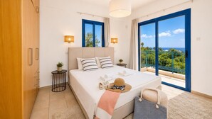 A bedroom with a bed, bedside tables, a hanging light, a view of the outdoors, and a balcony.