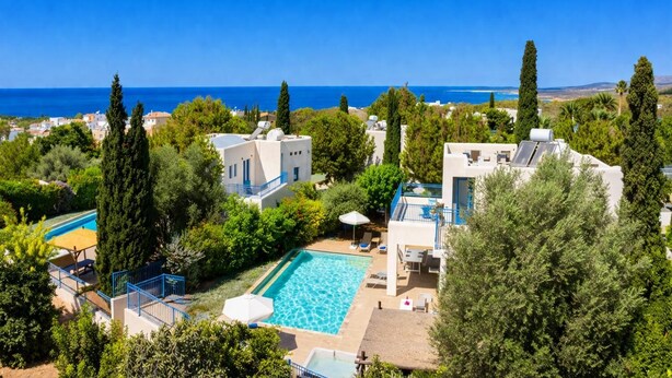 A resort with a swimming pool, multiple buildings, and a view of the sea.
