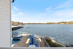 A balcony with blue lounge chairs and a pool, overlooking a calm body of water and distant buildings.