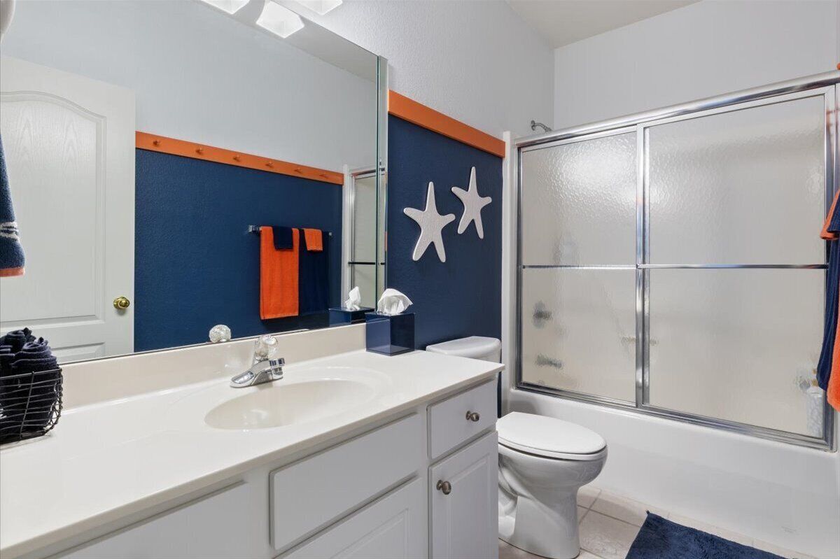A bathroom with a white sink, a mirror, a white toilet, and a glass shower enclosure.