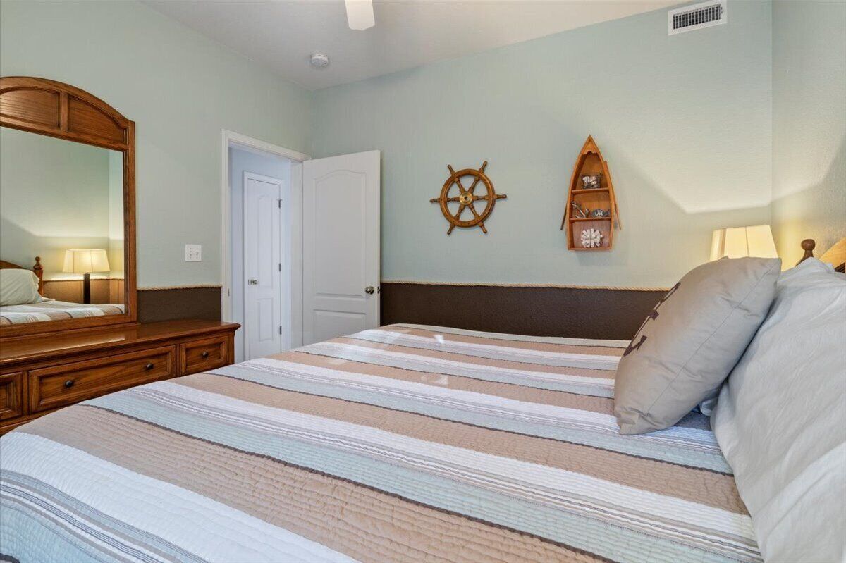 Ein Schlafzimmer mit Bett, Schminktisch, Spiegel, Tür und Wanddekorationen, darunter ein Schiffsschwester und ein Regal mit Gegenständen.