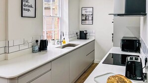 A modern kitchen with white cabinets, a sink, a coffee maker, a toaster, and a bread loaf on a tray. - Saltaire Mill Cottage (Saltaire, near Haworth)