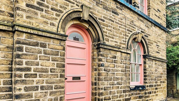 A stone building with a pink door and arched windows. - Saltaire Mill Cottage (Saltaire, near Haworth)