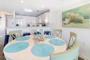 Un coin repas avec une table ronde, des sets de table bleus et des chaises de couleur claire.