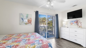 A bedroom with a bed, a TV, a balcony with a view, and a ceiling fan. - Bart’s Back River Retreat | Spacious 3BR Townhome | Water Views | South End (Tybee Island)