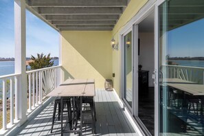 A covered outdoor area with a table and chairs, a railing, and a view of the water.