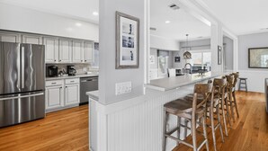 A modern kitchen with stainless steel appliances, white cabinetry, and a bar area with stools. - Large House w Pool Table, close Restaurants + Beach Access less than 1000 FT (Tybee Island)