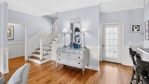 A hallway with a staircase, a white dresser with drawers, a mirror, and a door with a window. - Large House w Pool Table, close Restaurants + Beach Access less than 1000 FT (Tybee Island)