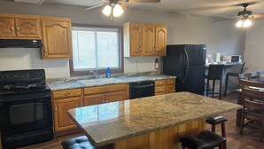 A kitchen with wooden cabinets, a granite countertop, a black stove, a refrigerator, and a ceiling fan.