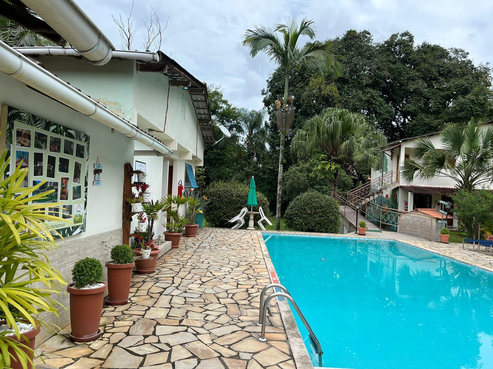Zona de piscina amb paviment de pedra, plantes en testos i una escala que condueix a un edifici.