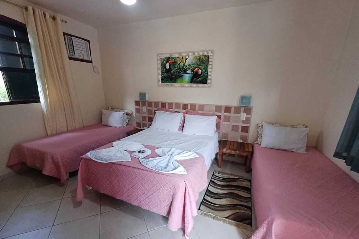 A hotel room with two single beds, a large bed, a window with curtains, a painting on the wall, and a tiled floor.