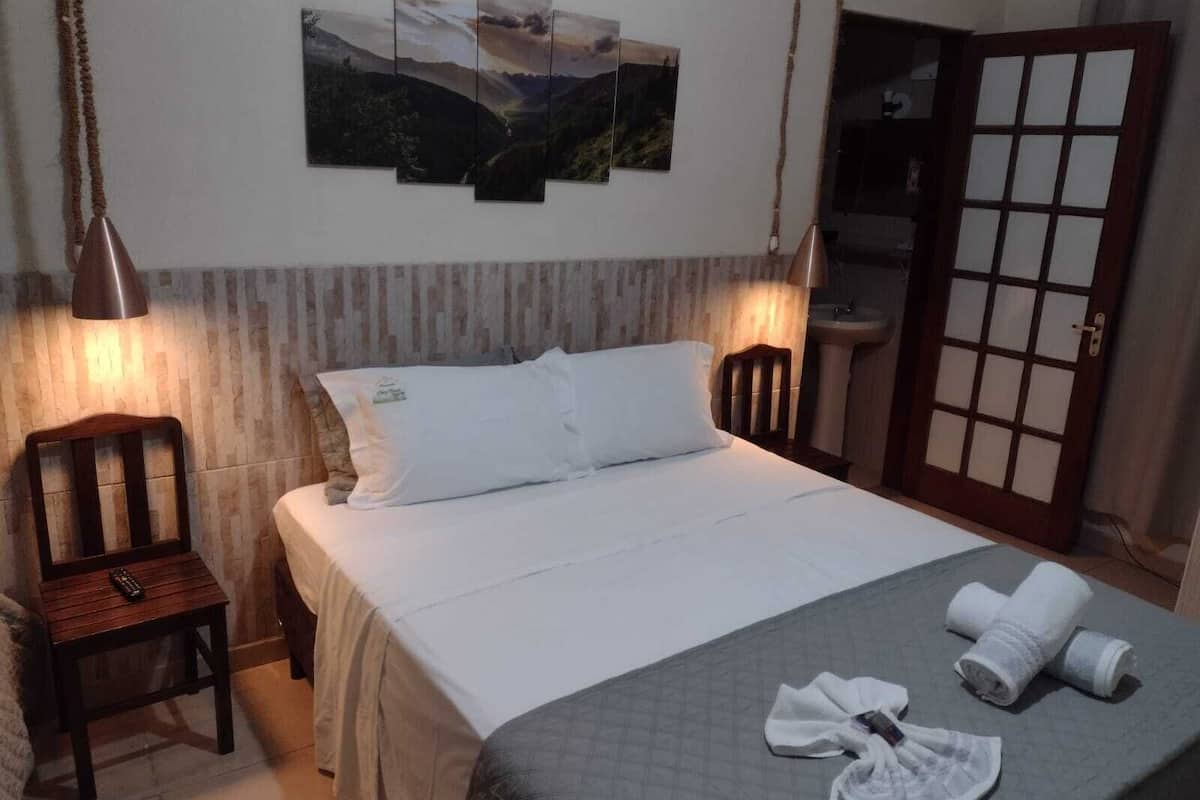 A bedroom with a bed, a chair, a desk, a sink, and a door.
