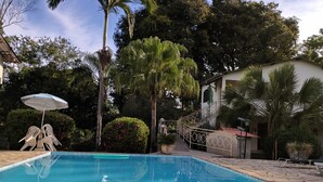 Une piscine à l’eau d’un bleu cristallin, entourée de palmiers et bordée d’un bâtiment blanc au toit rouge.