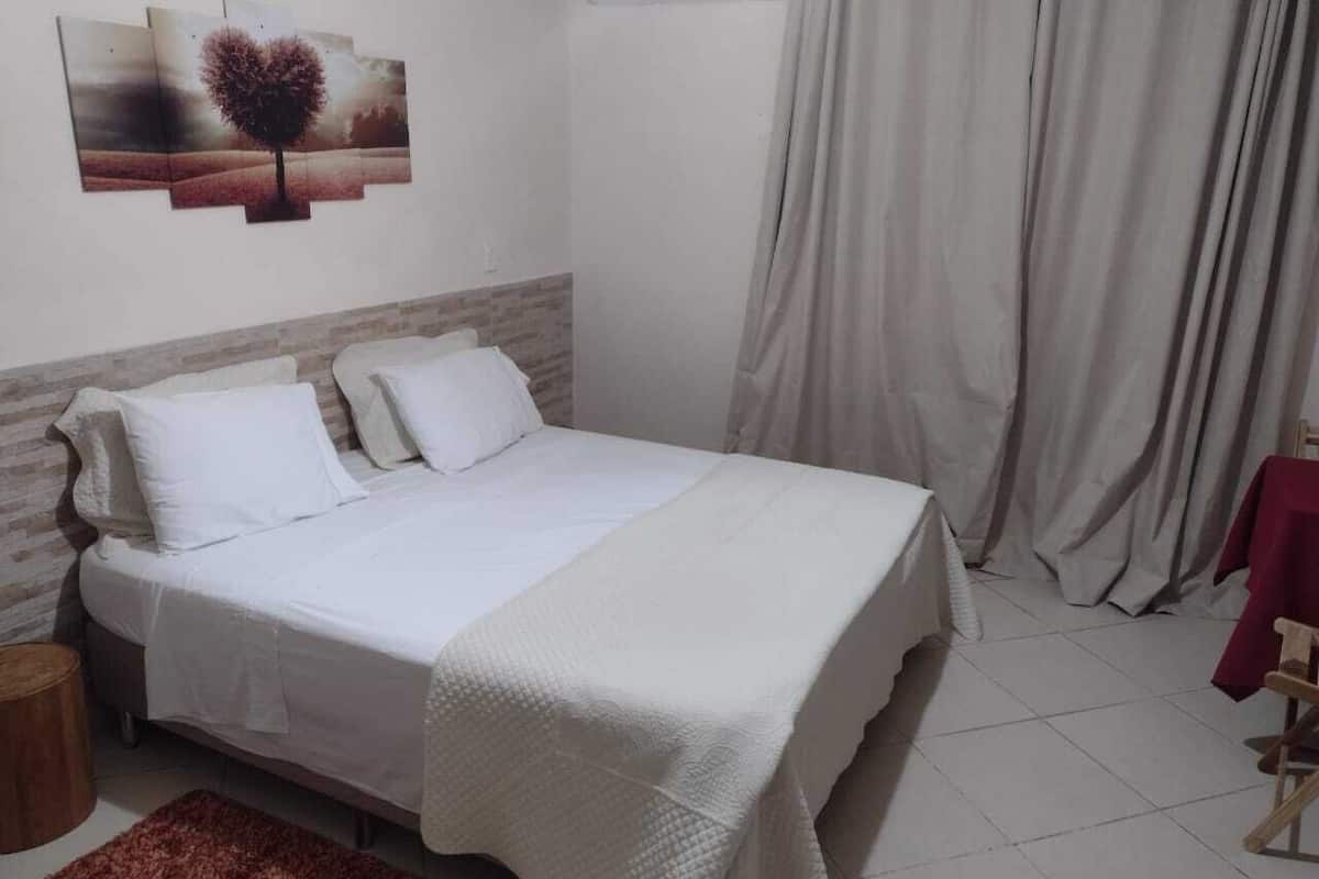 A neatly made bed with white linens, a wooden headboard, and a red rug.
