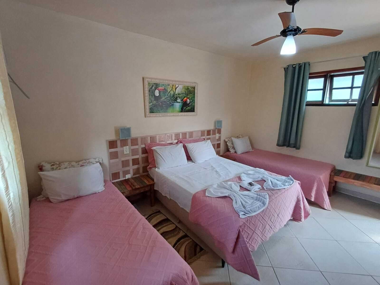 Quarto de hotel com duas camas de solteiro, um ventilador de teto, um quadro na parede e uma janela com cortinas.