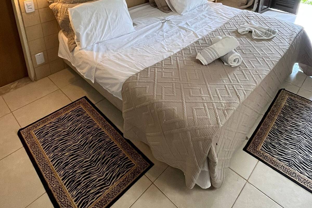 A neatly made bed with a patterned bedspread, two wall-mounted lamps, a painting of a landscape, and a door with a curtain.