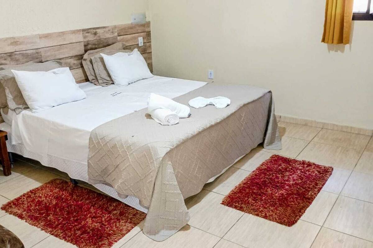 A bed with a wooden headboard, white bedding, and two red rugs.