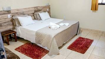 Cama com cabeceira de madeira, roupa de cama branca e dois tapetes vermelhos.