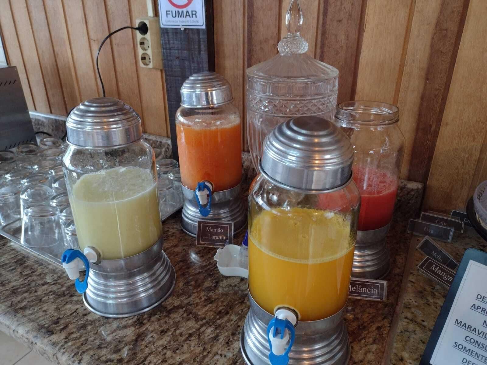 A beverage station with various drink dispensers, including a clear glass bottle with a metal cap and a metal jug with a spout.