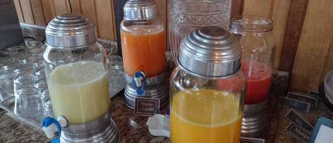 A beverage station with various drink dispensers, including a clear glass bottle with a metal cap and a metal jug with a spout.
