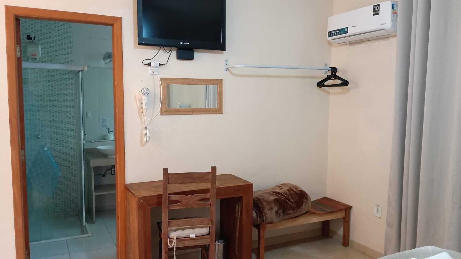 Una habitación con una mesa de madera, un banco, un televisor, un espejo y un equipo de aire acondicionado.
