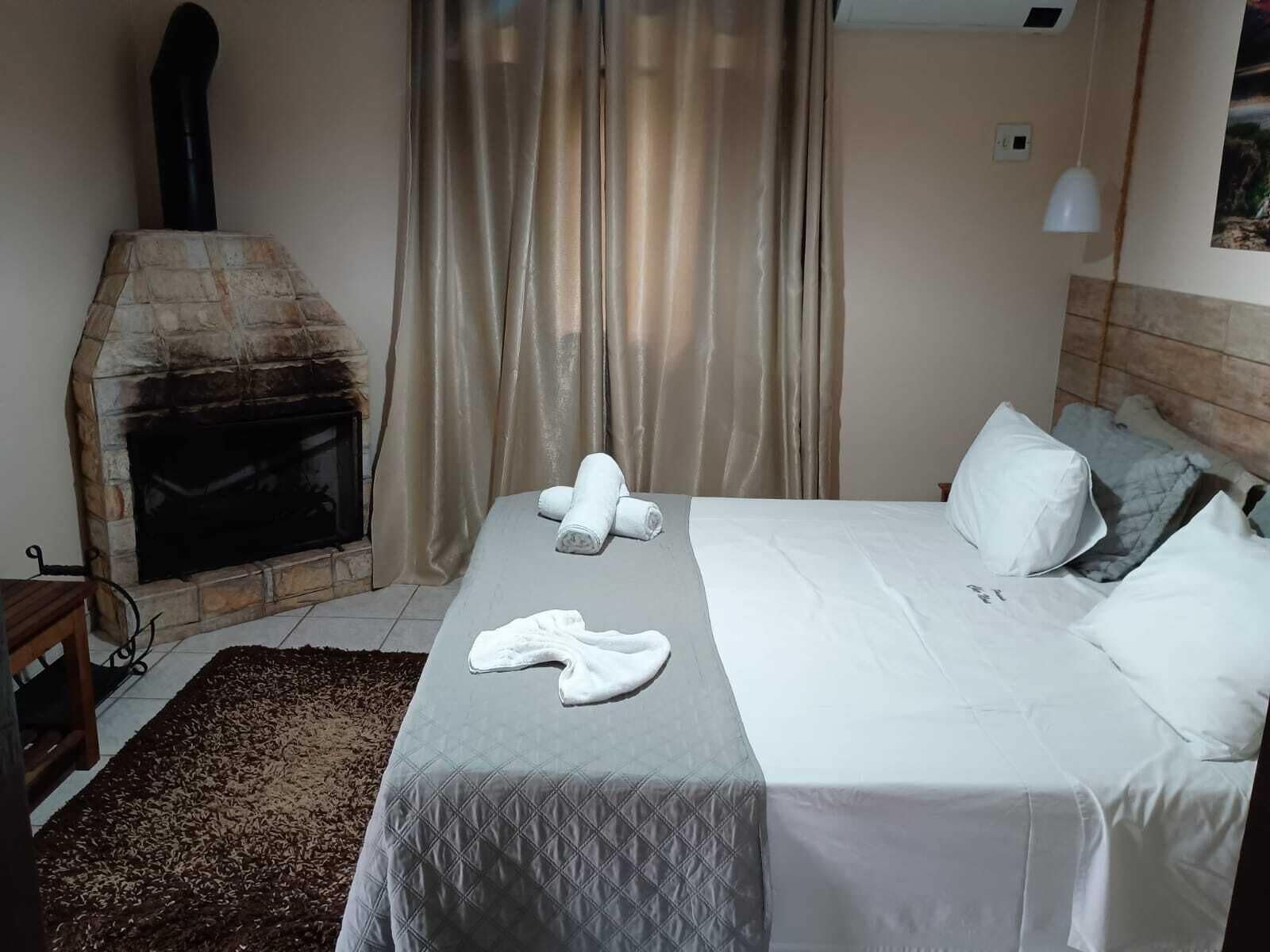 Habitación de hotel con chimenea de piedra, cama con ropa blanca, alfombra marrón y ventana con cortinas color beige.