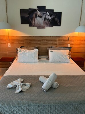 A hotel room with a large bed, two nightstands, a wooden headboard, and a wall-mounted artwork of horses. - Pousada chez Nous  (Itatiaia)