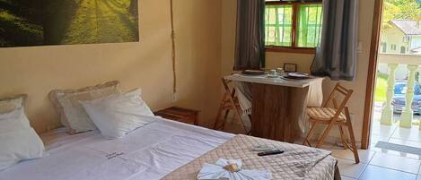 Habitación de hotel con cama, una mesa de comedor con sillas, un cuadro en la pared y vistas al exterior a través de una ventana.