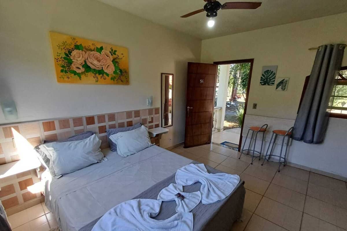 A bedroom with a bed, a ceiling fan, a door leading outside, and a painting on the wall.