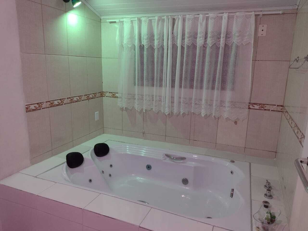 A bathroom with a large bathtub, a shower area, and a window with a lace curtain.
