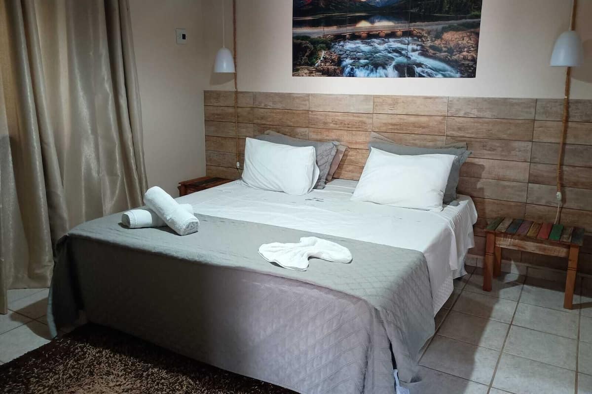 A hotel room with a bed, a painting of a landscape, a nightstand, and a lamp.