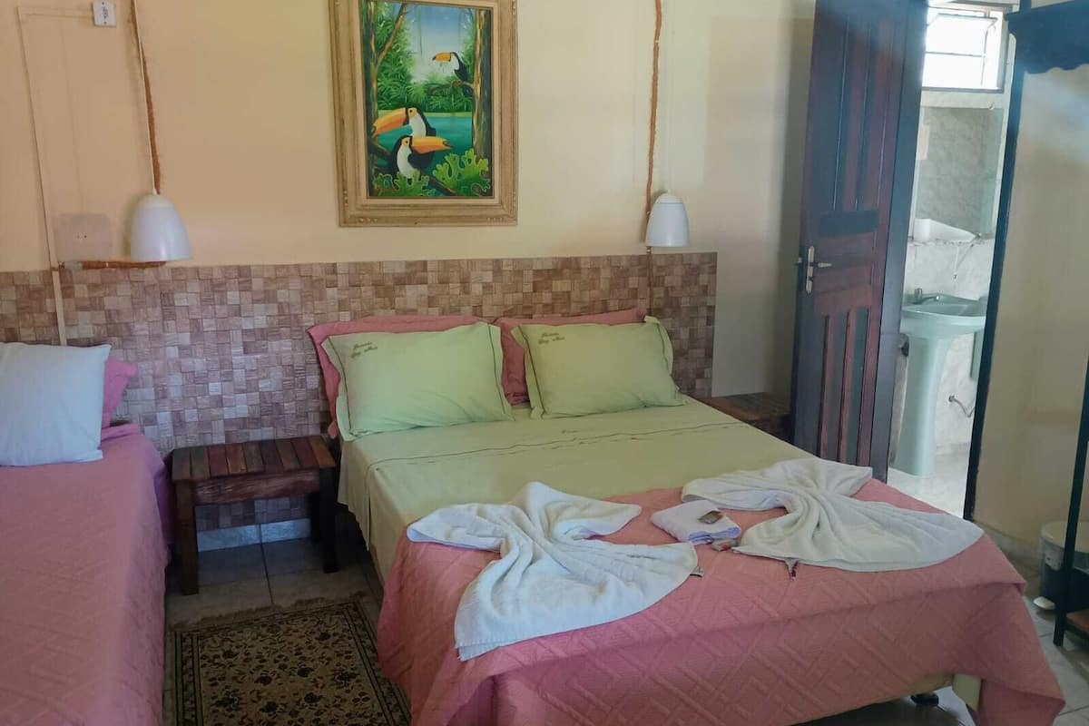 A hotel room with a bed, a nightstand, a painting, and a bathroom visible through an open door.