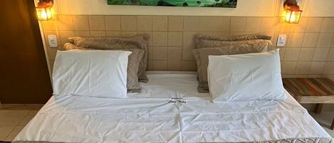 Habitación de hotel con cama, dos almohadas, un cuadro de un paisaje y dos lámparas de pared.