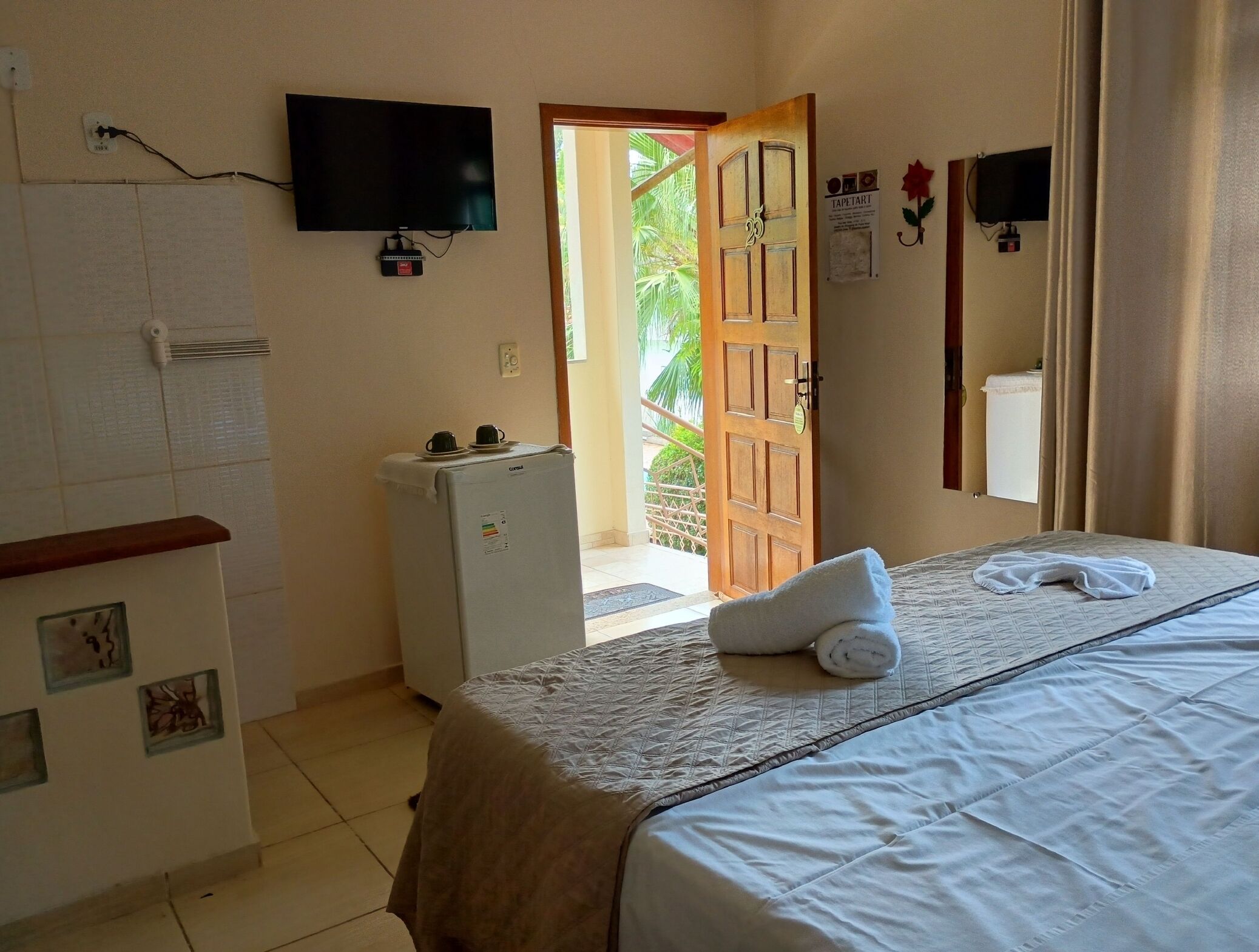 A hotel room with a bed, a television, a refrigerator, and a door leading to a balcony.