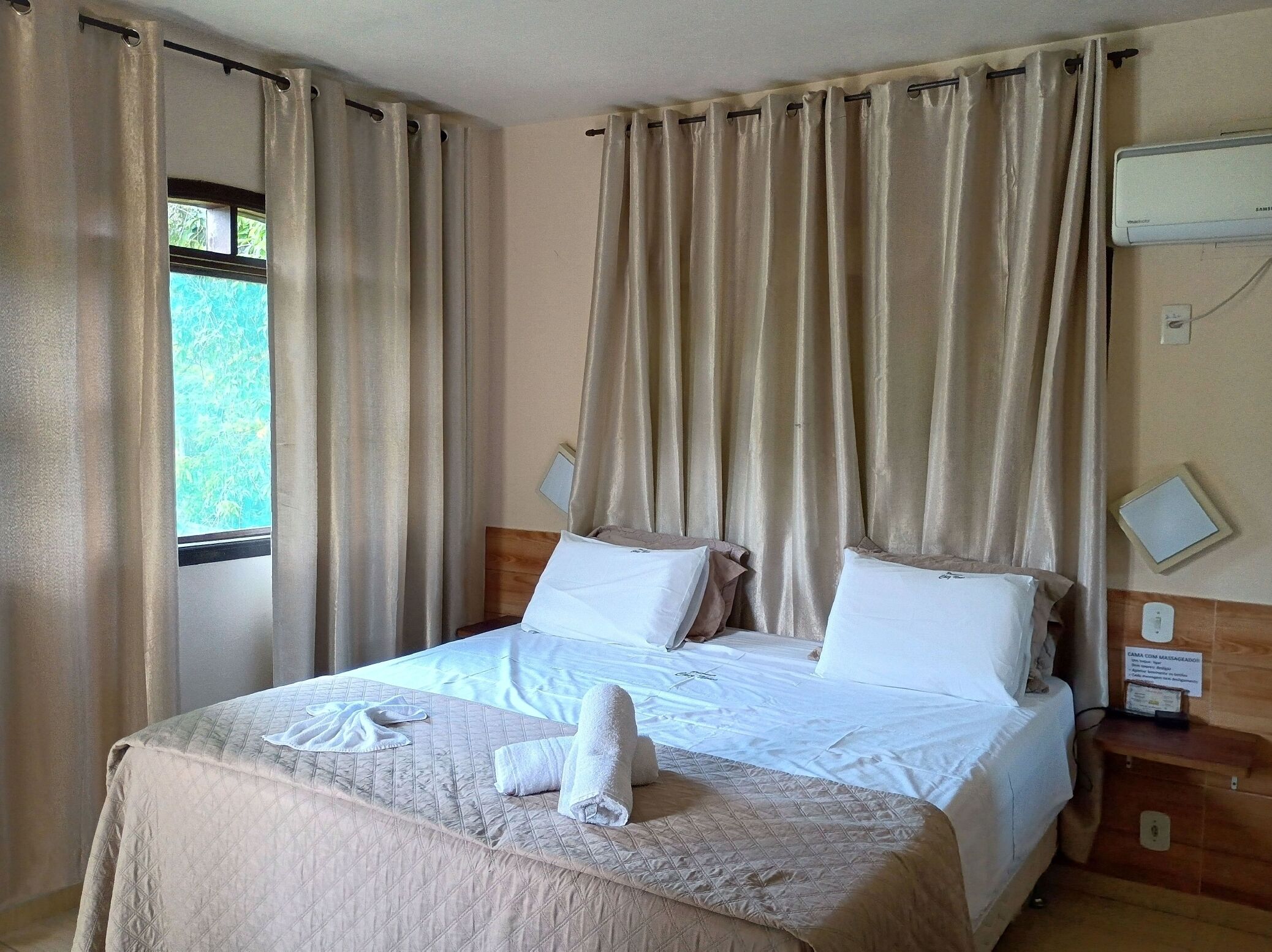 Ein Hotelzimmer mit Bett, Vorhängen, einer wandmontierten Klimaanlage und einem Fenster mit Blick.