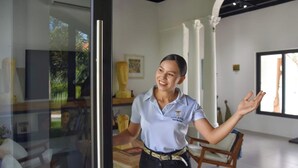 A person in a light blue shirt with a logo, standing in a room with a glass door, white walls, and a wooden chair. - Casa Roma - Luxury Villa (El Tamarindo)