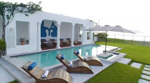 A poolside area with lounge chairs, a pergola, and a view of the pool.