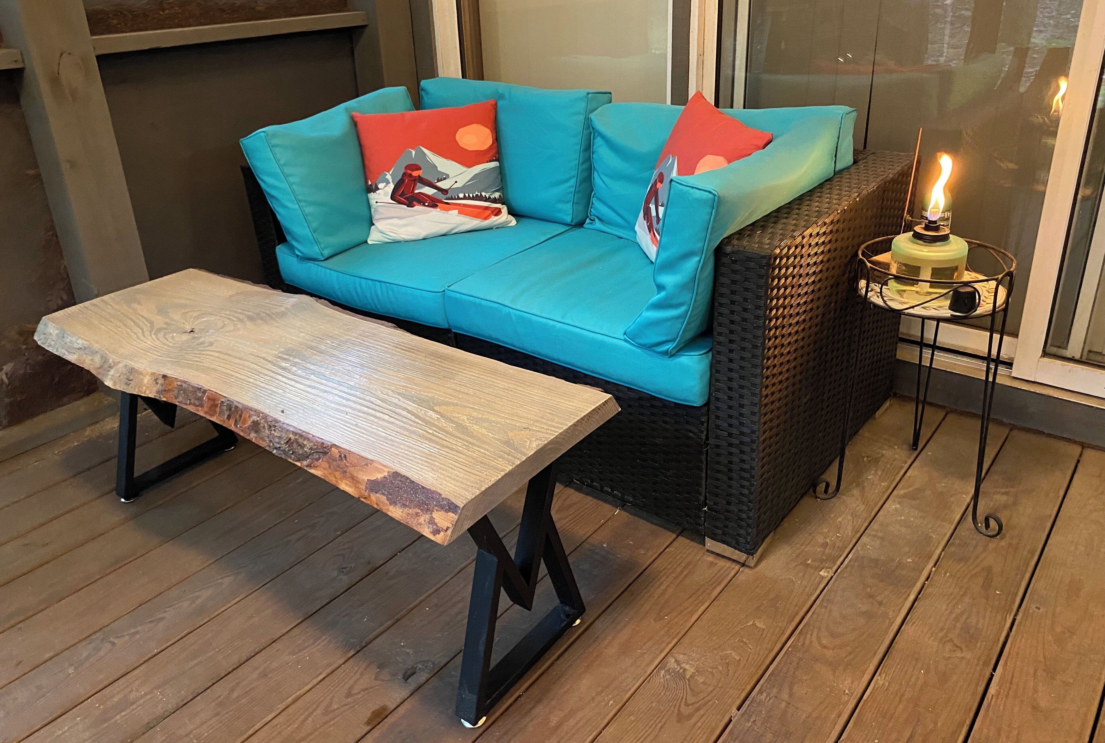 Un canapé de couleur bleu sarcelle agrémenté de coussins rouges et blancs, un banc en bois et une table avec une bougie.