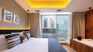 A modern bedroom with a large bed, a view of the city, and a wooden vanity.