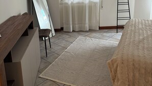 A bedroom with a bed, a wooden dresser, a mirror, a window with blinds, a radiator, and a ladder. - MADDY'S HOUSE Spacious apartment furnished with care and originality  (Mandello del Lario)