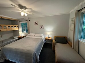 Ein Schlafzimmer mit Etagenbett, einem Einzelbett, einem Nachttisch mit Lampe, einem Fenster mit Vorhängen und einem Deckenventilator.