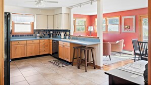 A kitchen with wooden cabinets, a blue countertop, and a ceiling fan. There are two bar stools and a table with papers.